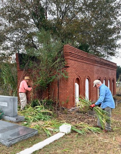 Volunteers clearing brush beside a brick family plot