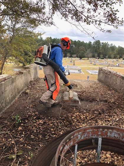 Volunteer raking debris between graves